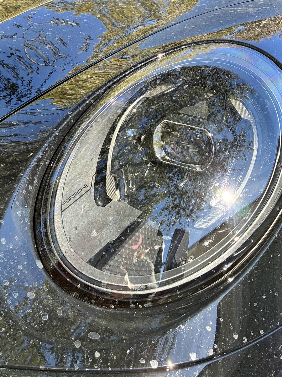 Black Porsche 911 hood and headlight covered in dried hard-water spots before washing