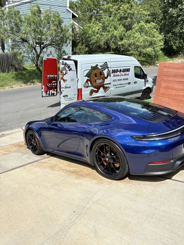 Drip-N-Shine mobile car wash van set up in a residential driveway with equipment ready, washing a blue Porsche